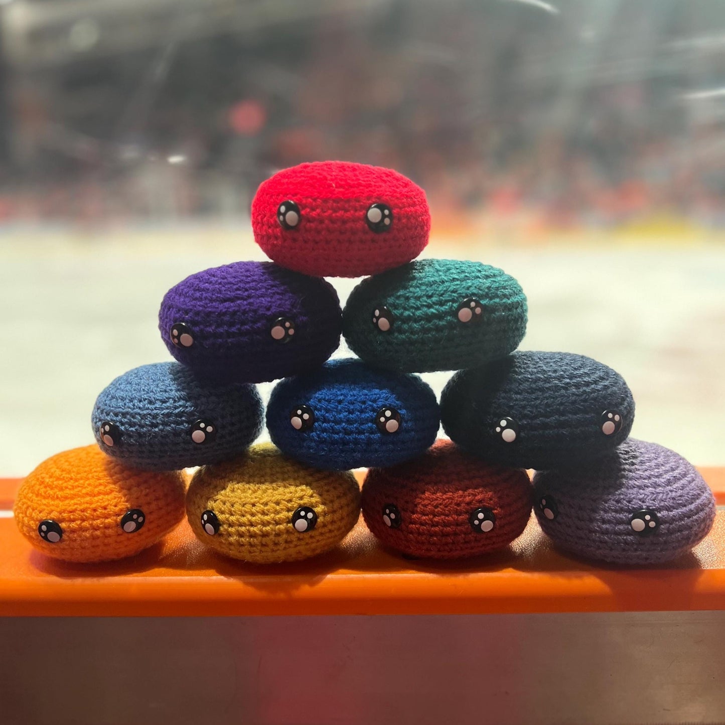 All EIHL team colour crochet ice hockey pucks in a pyramid in front of an ice rink