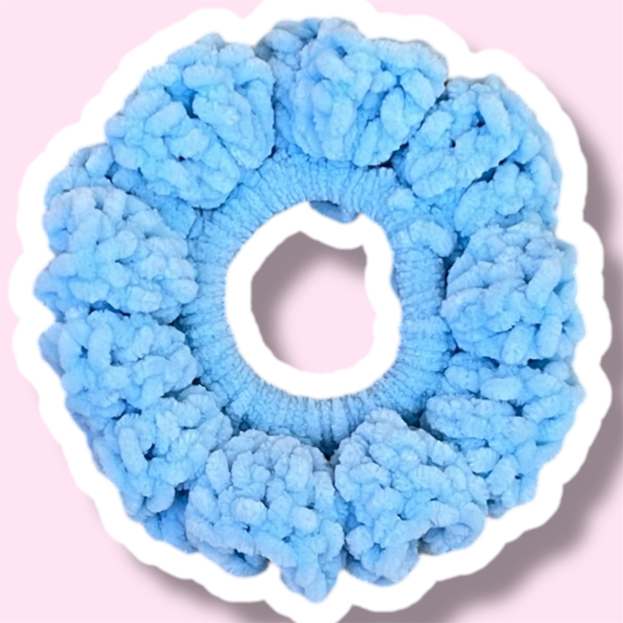 Close up image of a baby blue handmade crochet scrunchie on a light pink background
