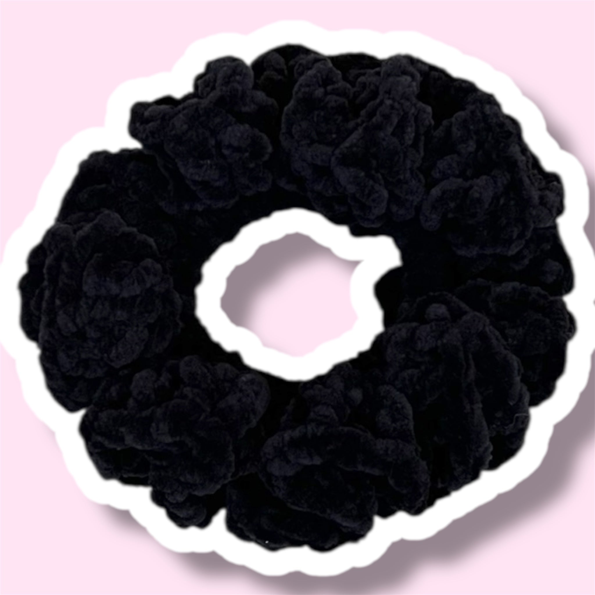 Close up image of a black handmade crochet scrunchie on a light pink background