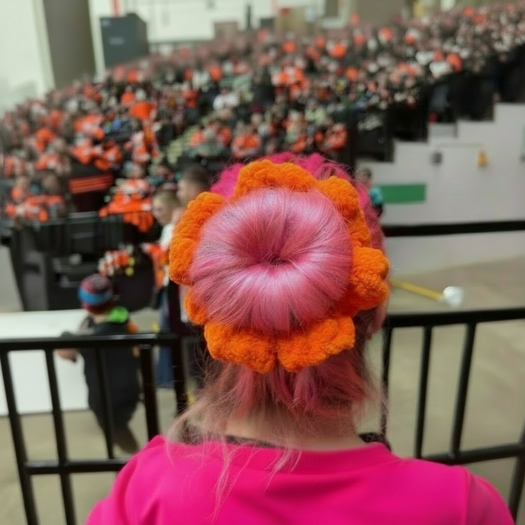 Person wearing an orange sheffield steelers colour themed scrunchie sitting in the stands of an ice hockey game