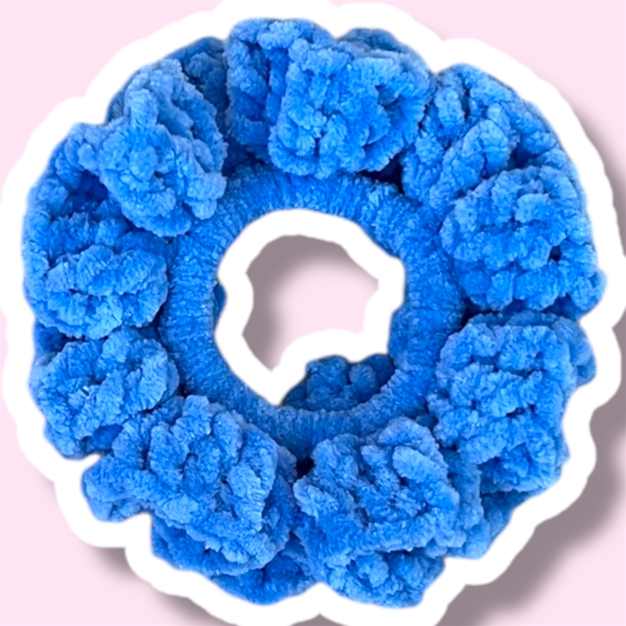 Close up image of a cobalt blue handmade crochet scrunchie on a light pink background