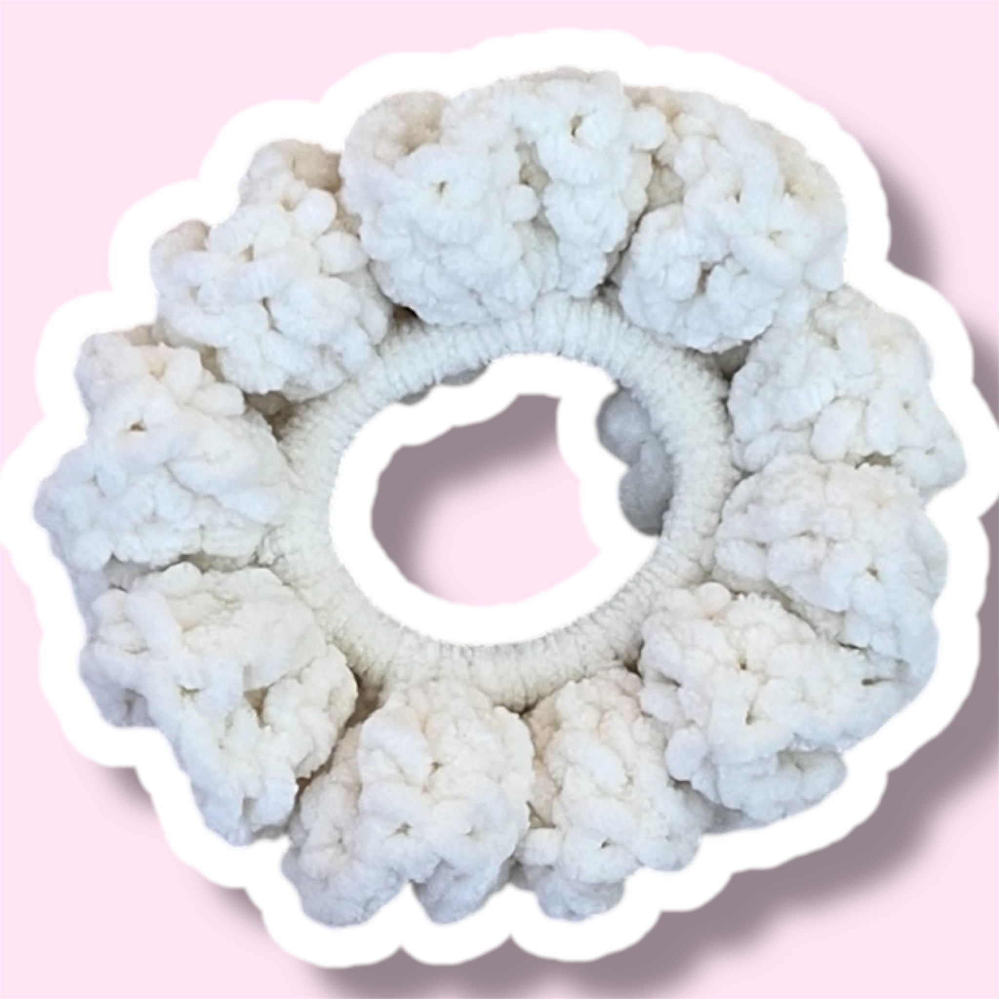 Close up image of a cream handmade crochet scrunchie on a light pink background