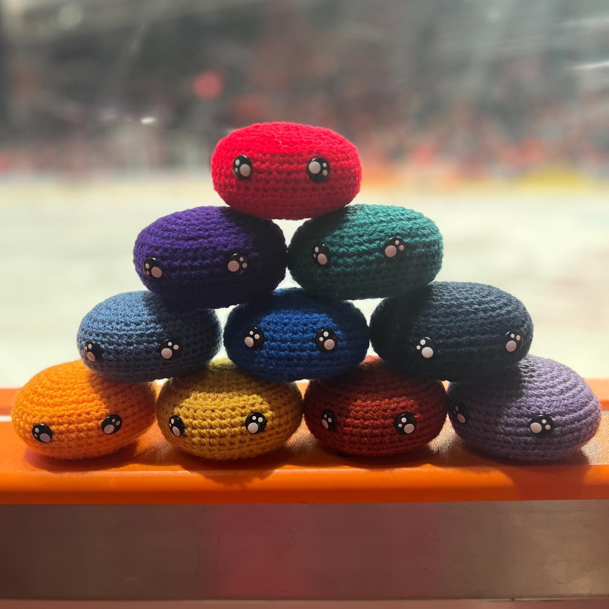 All EIHL team colour crochet ice hockey pucks in a pyramid in front of an ice rink 