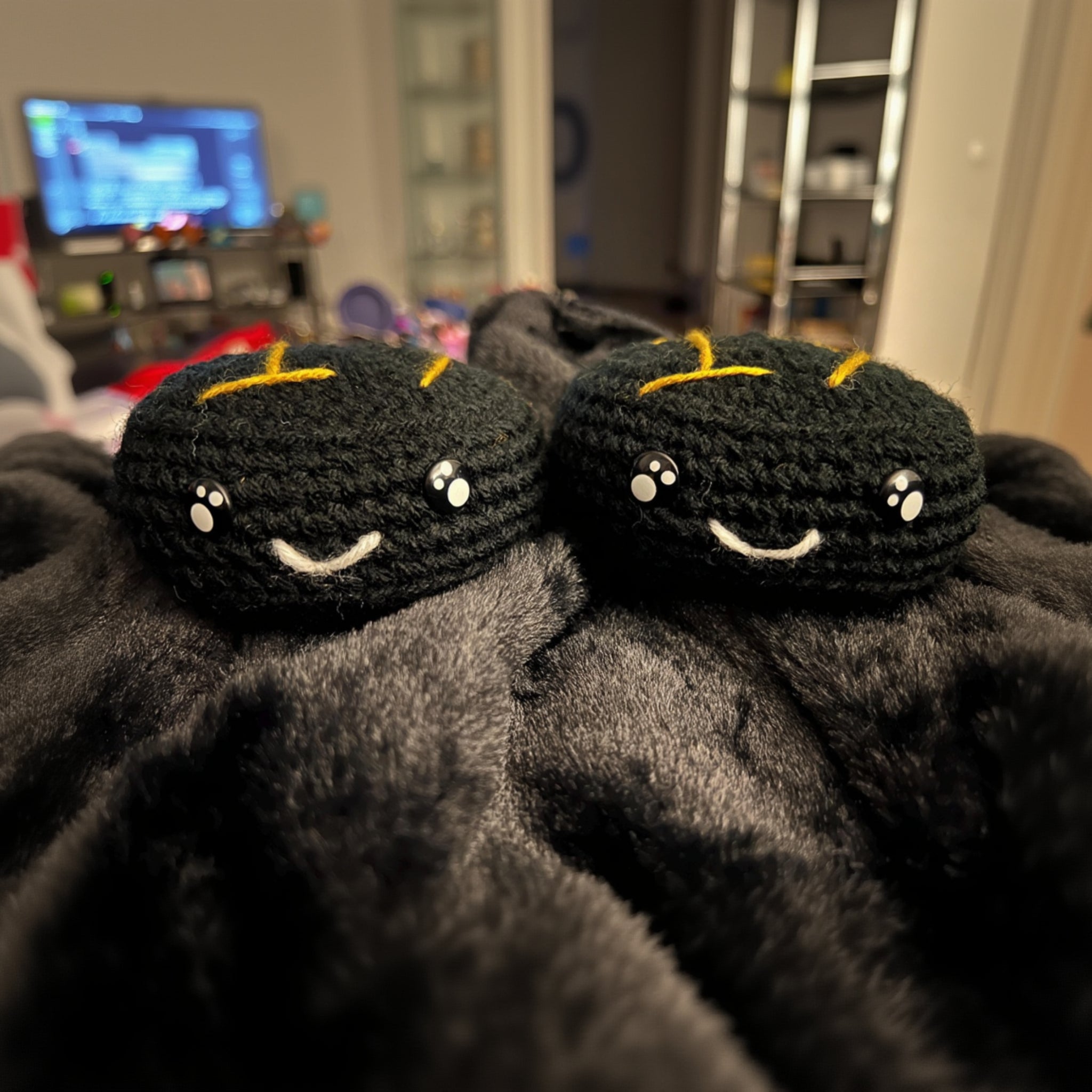 Two black crochet ice hockey puck plush with nottingham panthers ice hockey team themed colour stitching sitting on a black blanket