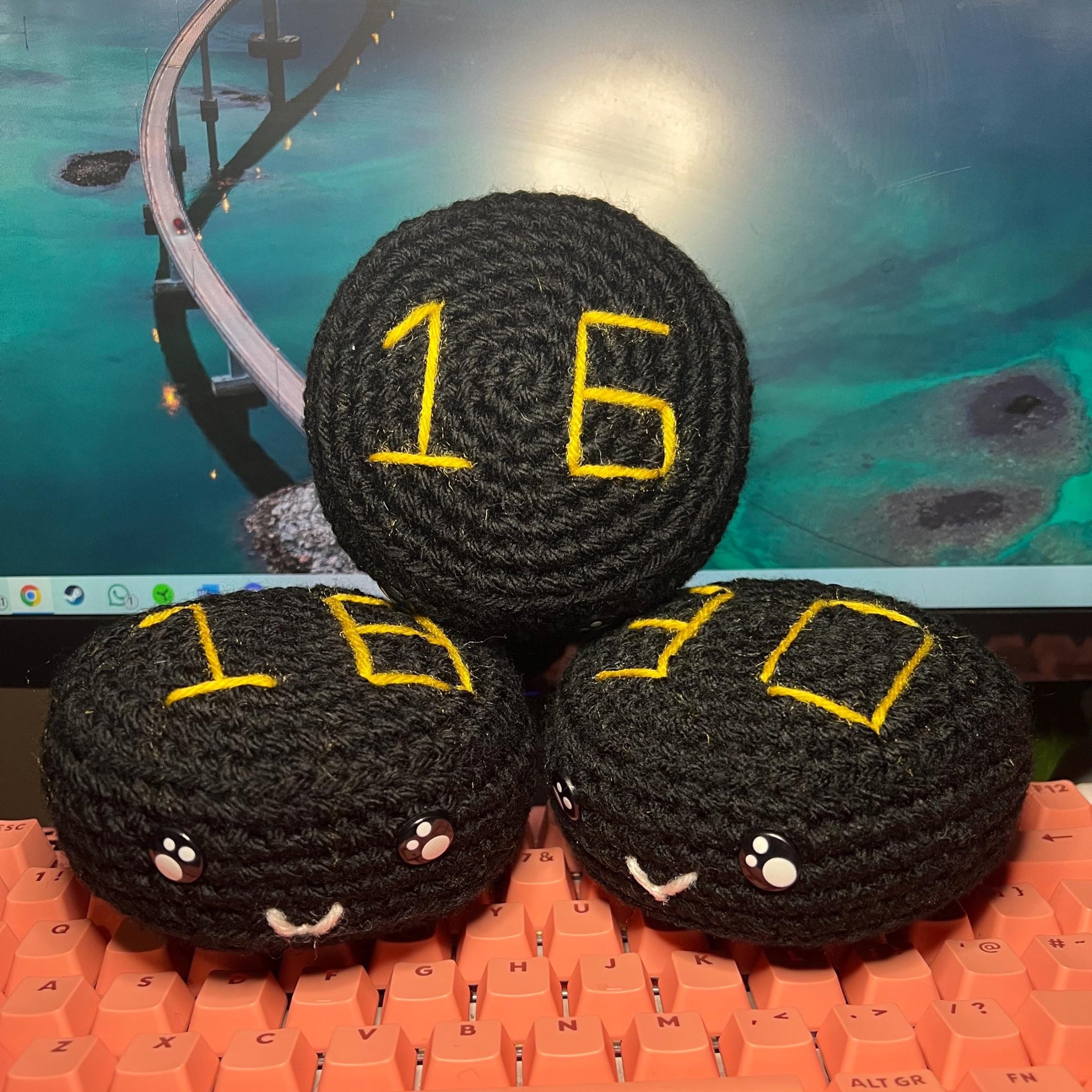 Three crochet black puck plush with nottingham panthers themed colour stitching sitting on a keyboard resting against a computer