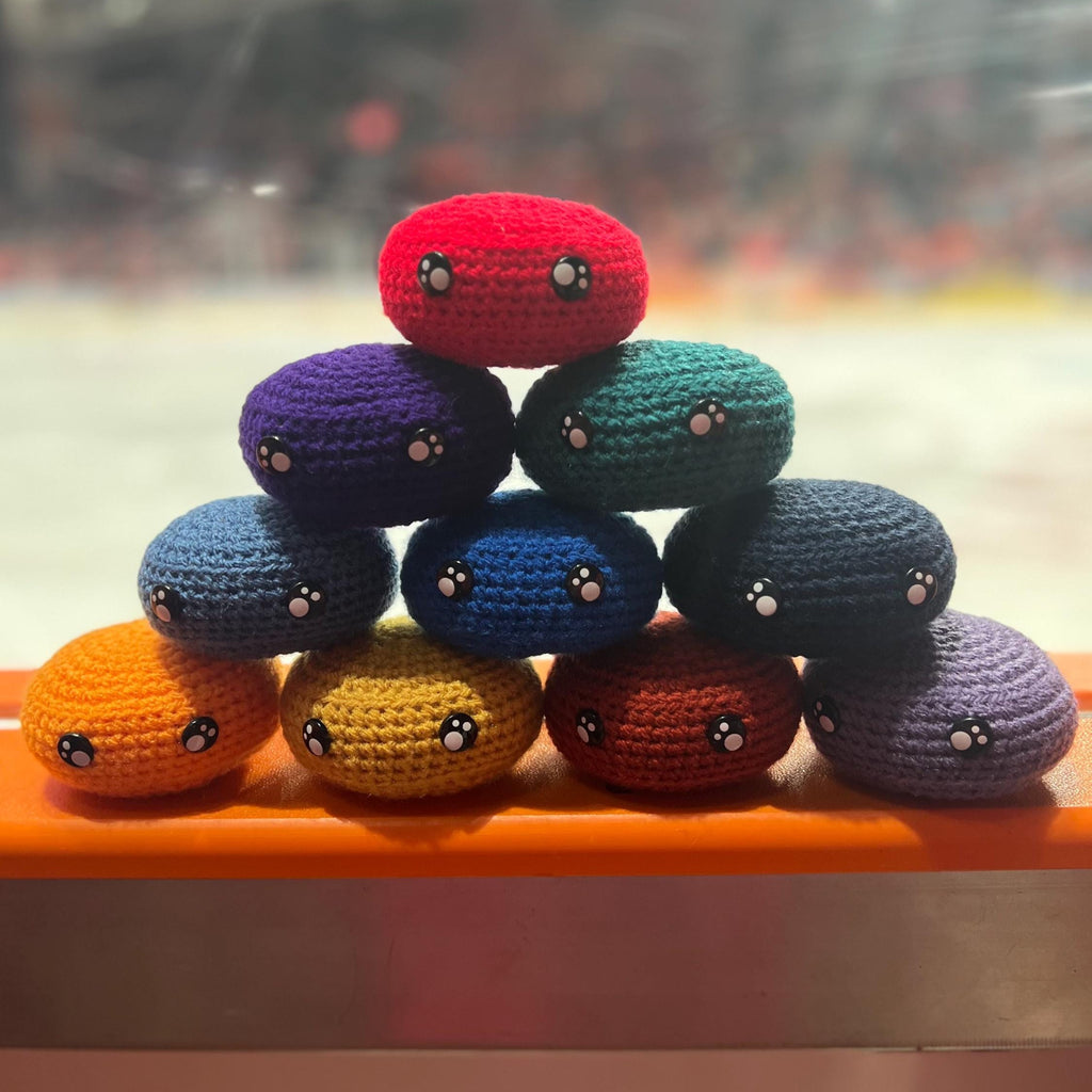 All EIHL team colour crochet ice hockey pucks in a pyramid in front of an ice rink 