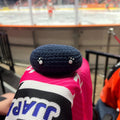 Person holding a dundee stars colour themed blue crochet ice hockey puck in front of an ice rink