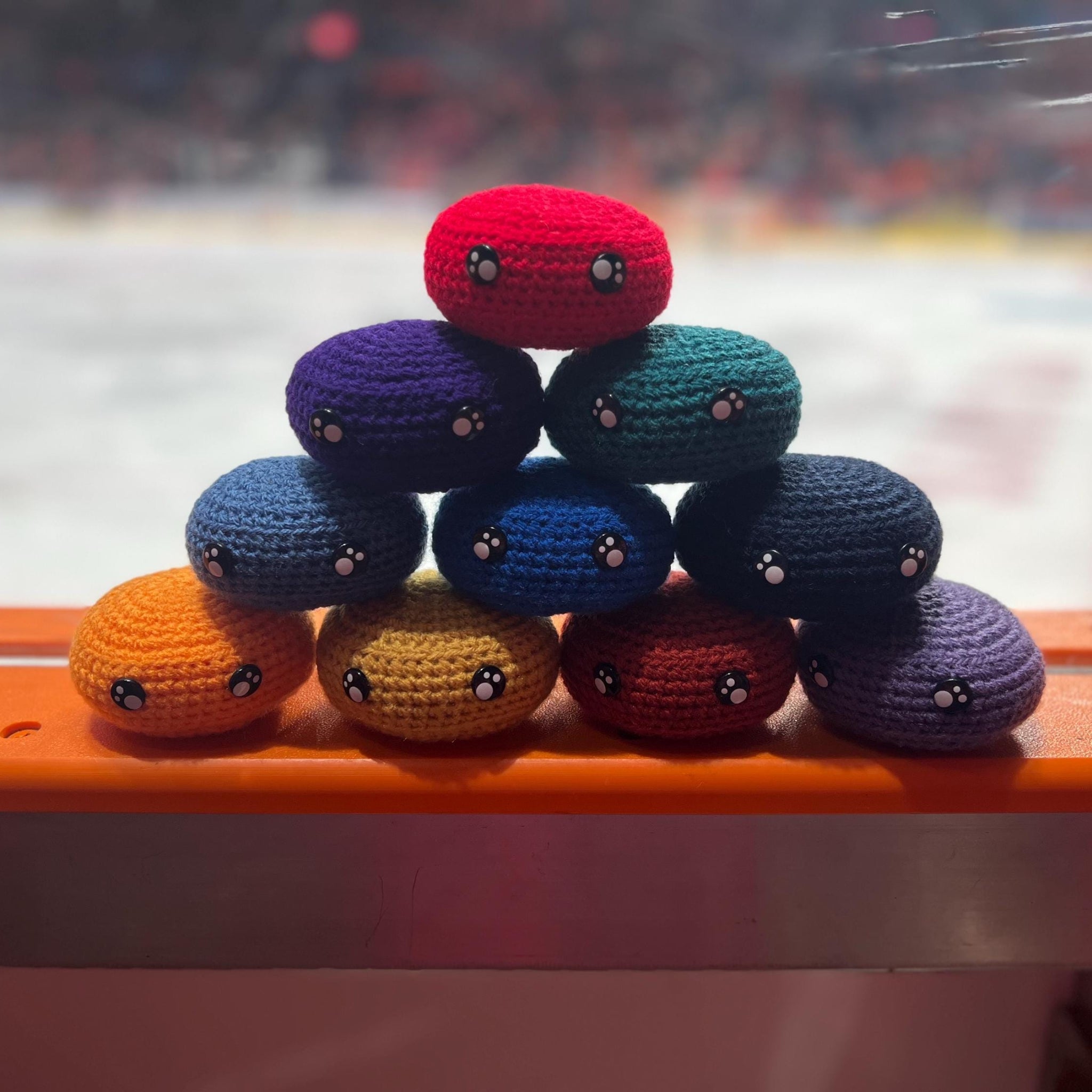 All EIHL team colour crochet ice hockey pucks in a pyramid in front of an ice rink 
