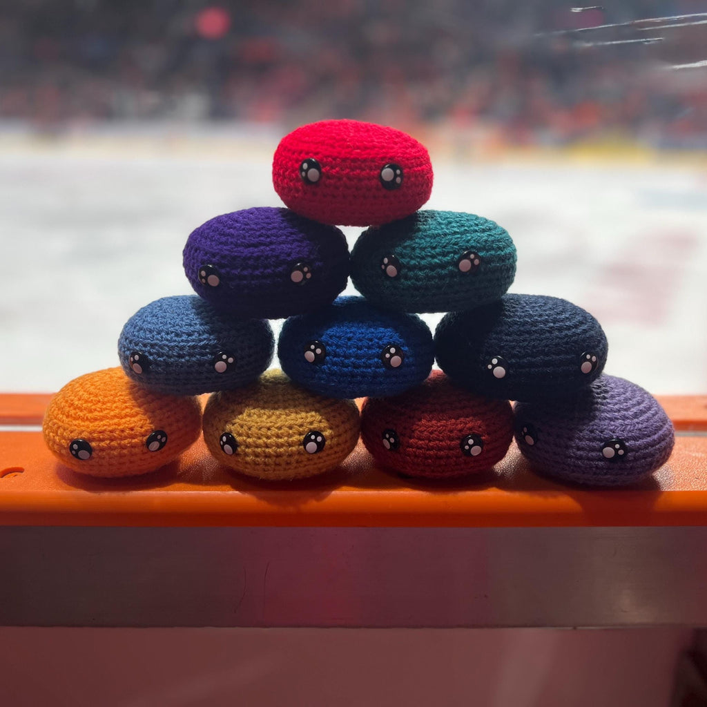 All EIHL team colour crochet ice hockey pucks in a pyramid in front of an ice rink 