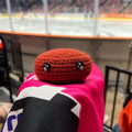 Person holding a guildford flames dark red colour themed crochet ice hockey puck in front of an ice rink