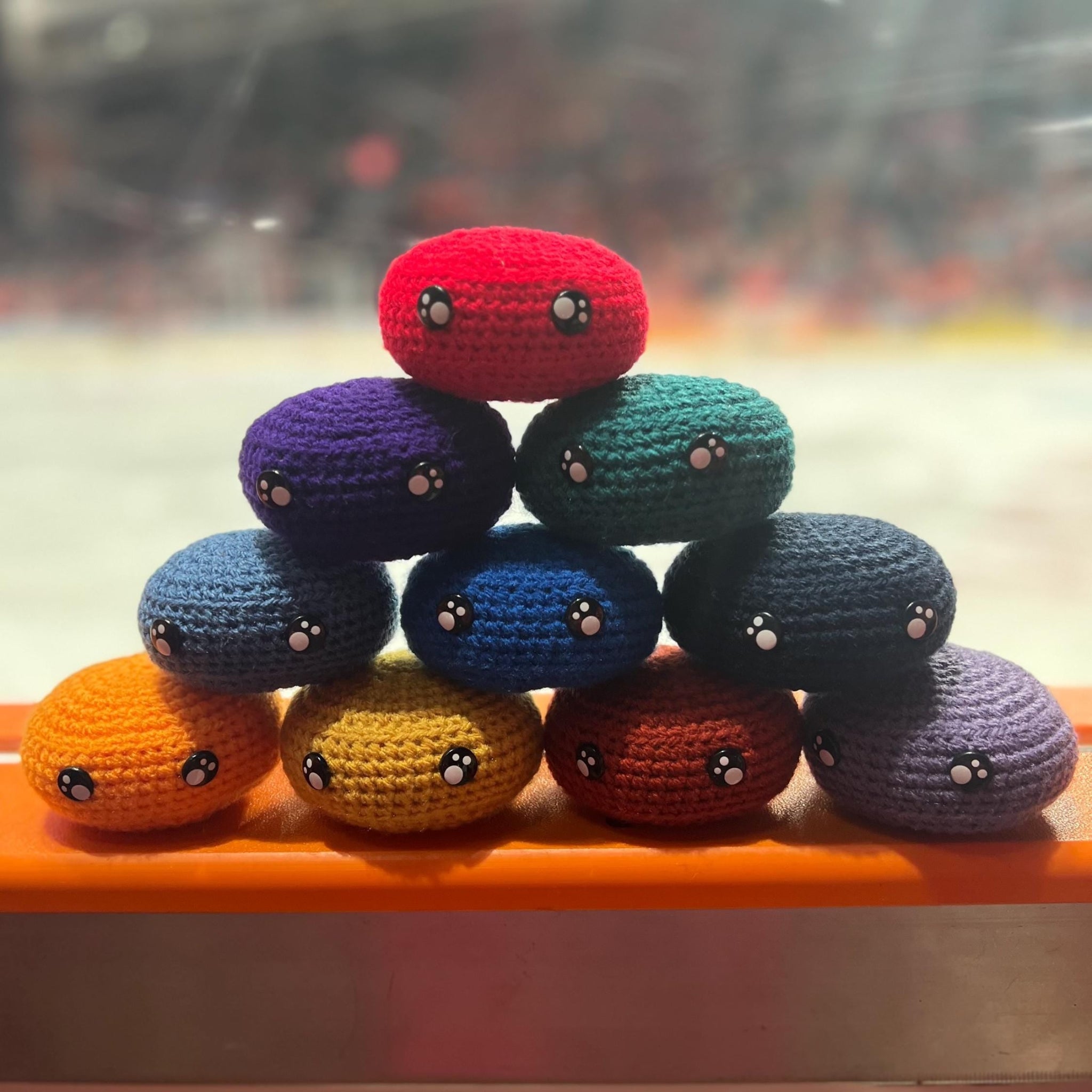 All EIHL team colour crochet ice hockey pucks in a pyramid in front of an ice rink 