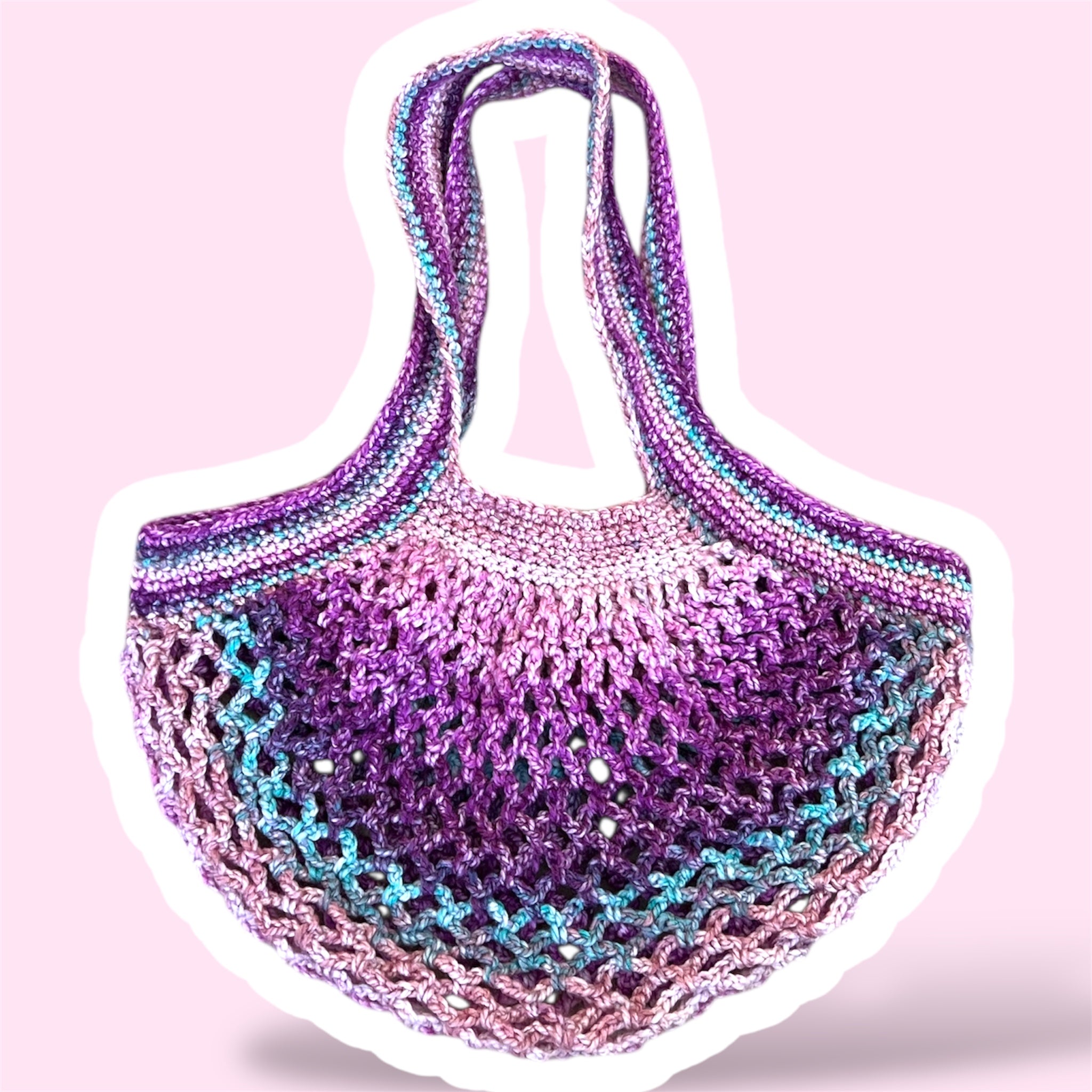 A picture of a purple and pink handmade crochet mesh market bag on a plain light pink background