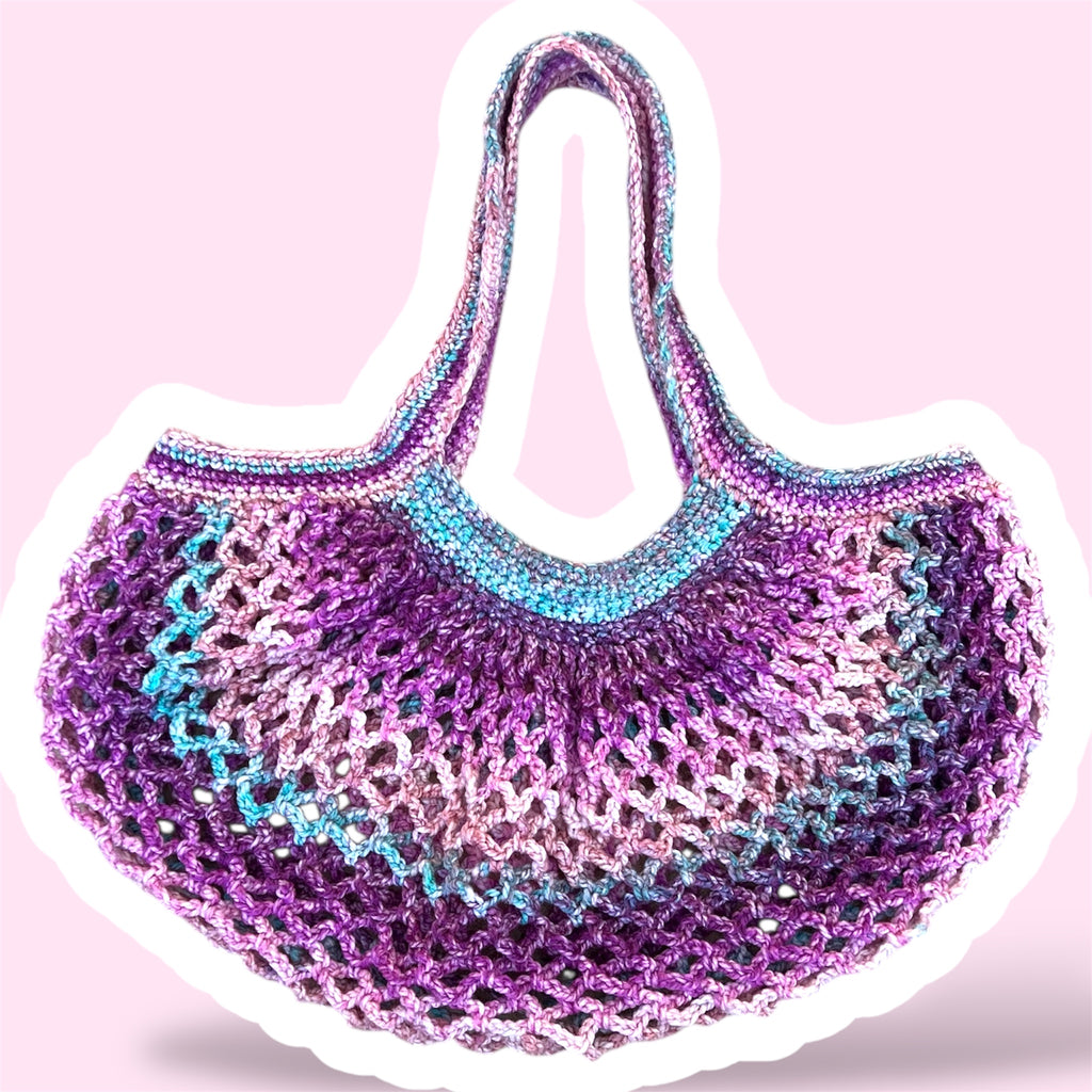 A picture of a purple and pink handmade crochet mesh market bag on a plain light pink background