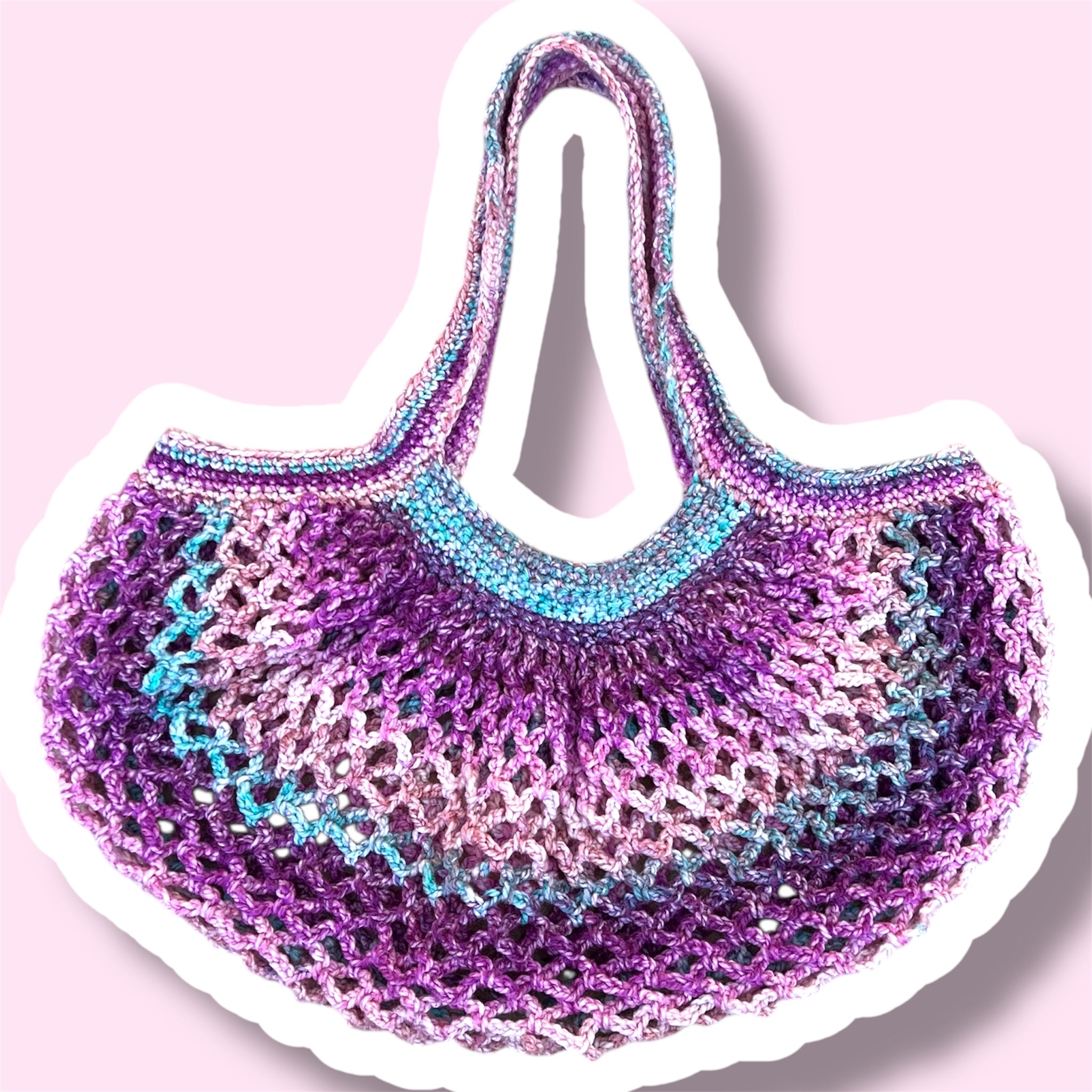 A picture of a purple and pink handmade crochet mesh market bag on a plain light pink background