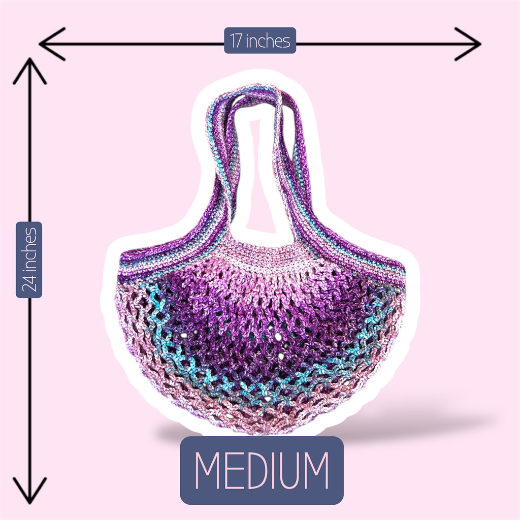 A picture of a purple and pink handmade crochet mesh market bag on a plain light pink background showing the size of the medium version of this bag