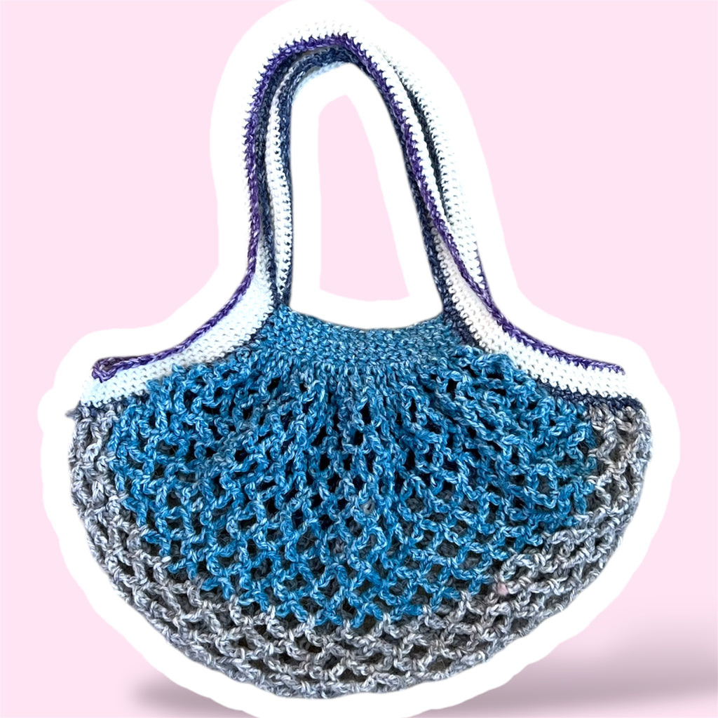 Crochet mesh market bag in blue grey white and purple gradients on a light pink background