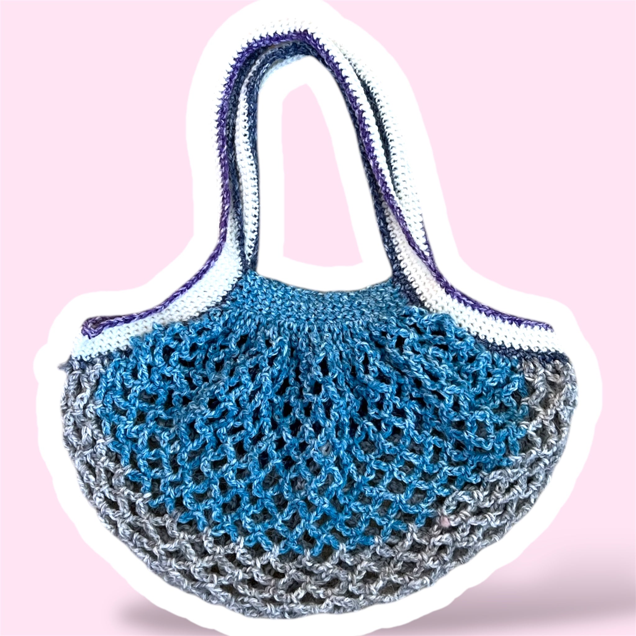 Crochet mesh market bag in blue grey white and purple gradients on a light pink background