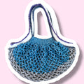 Crochet mesh market bag in blue grey white and purple gradients on a light pink background