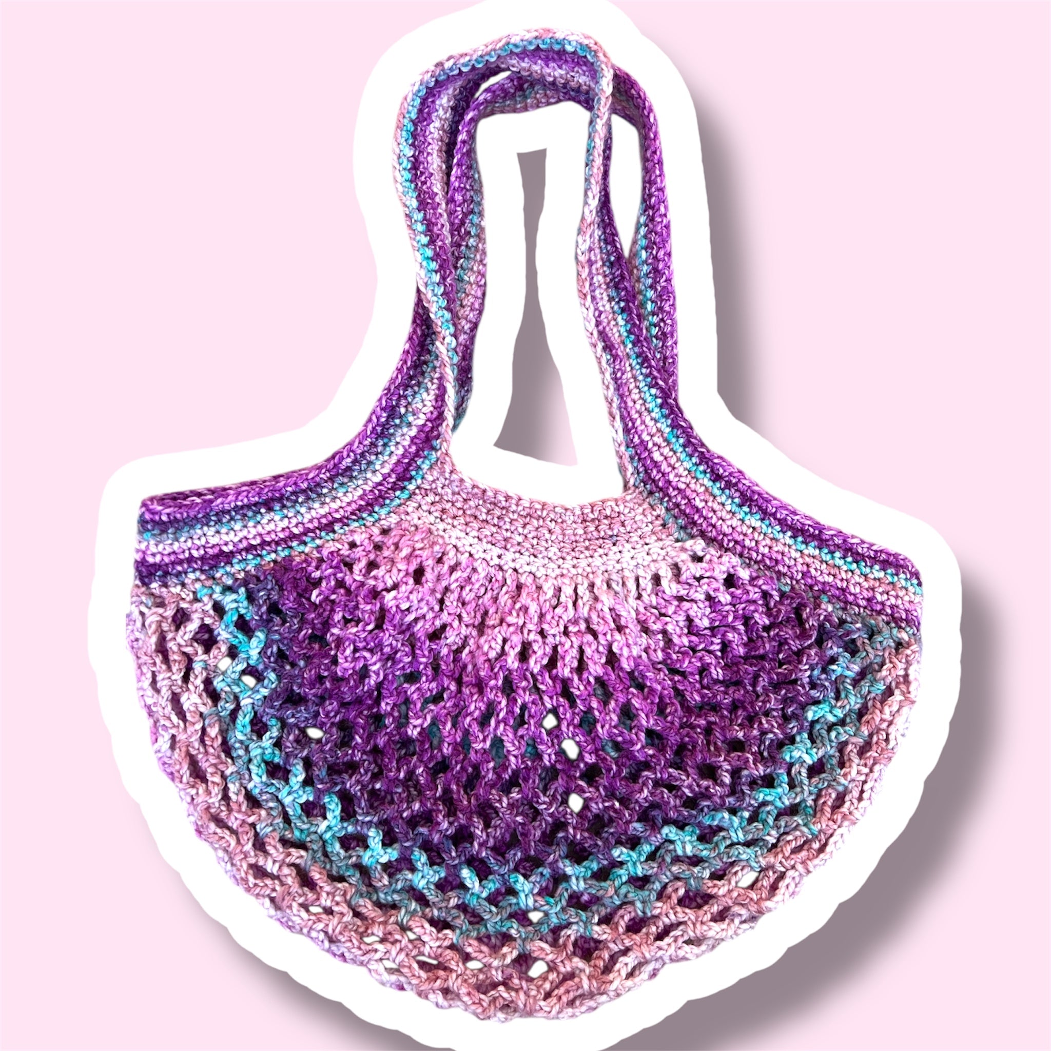A picture of a purple and pink handmade crochet mesh market bag on a plain light pink background