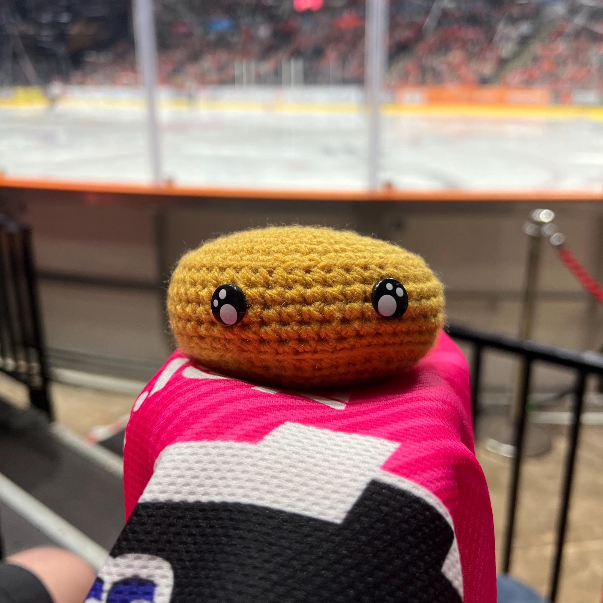 Person holding a nottingham panthers gold colour themed crochet ice hockey puck in front of an ice rink