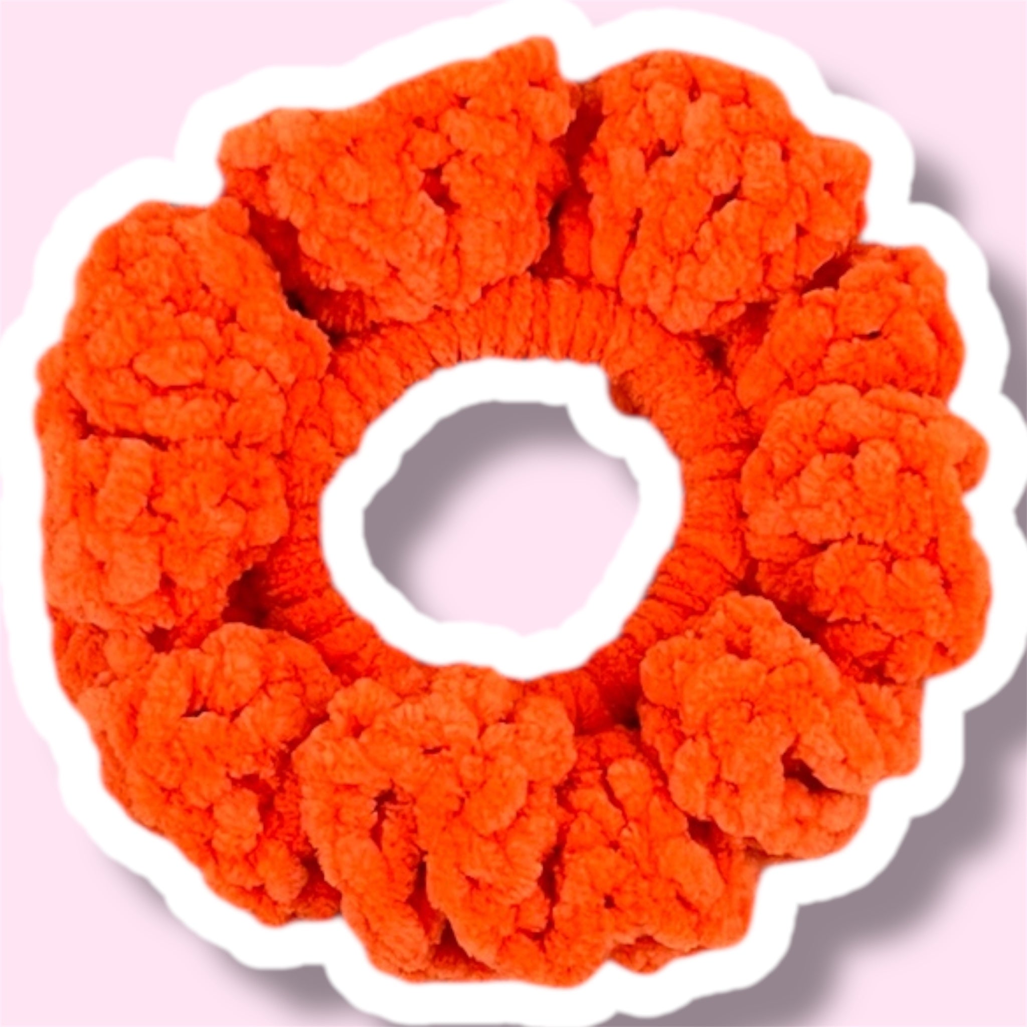 Close up image of an orange handmade crochet scrunchie on a light pink background