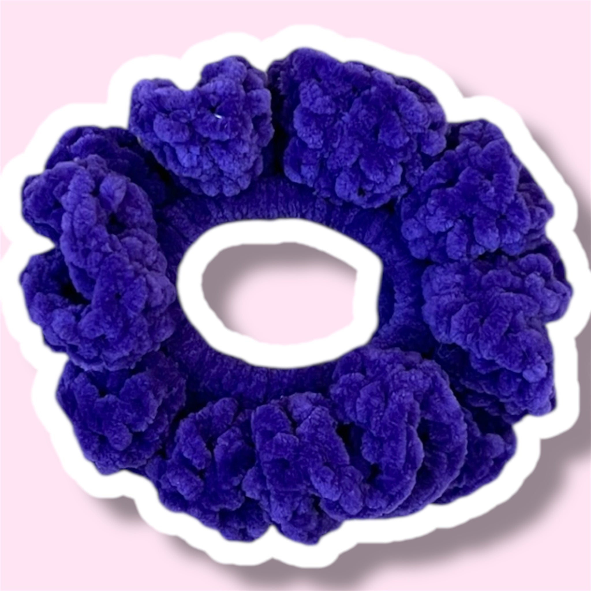Close up image of a purple handmade crochet scrunchie on a light pink background