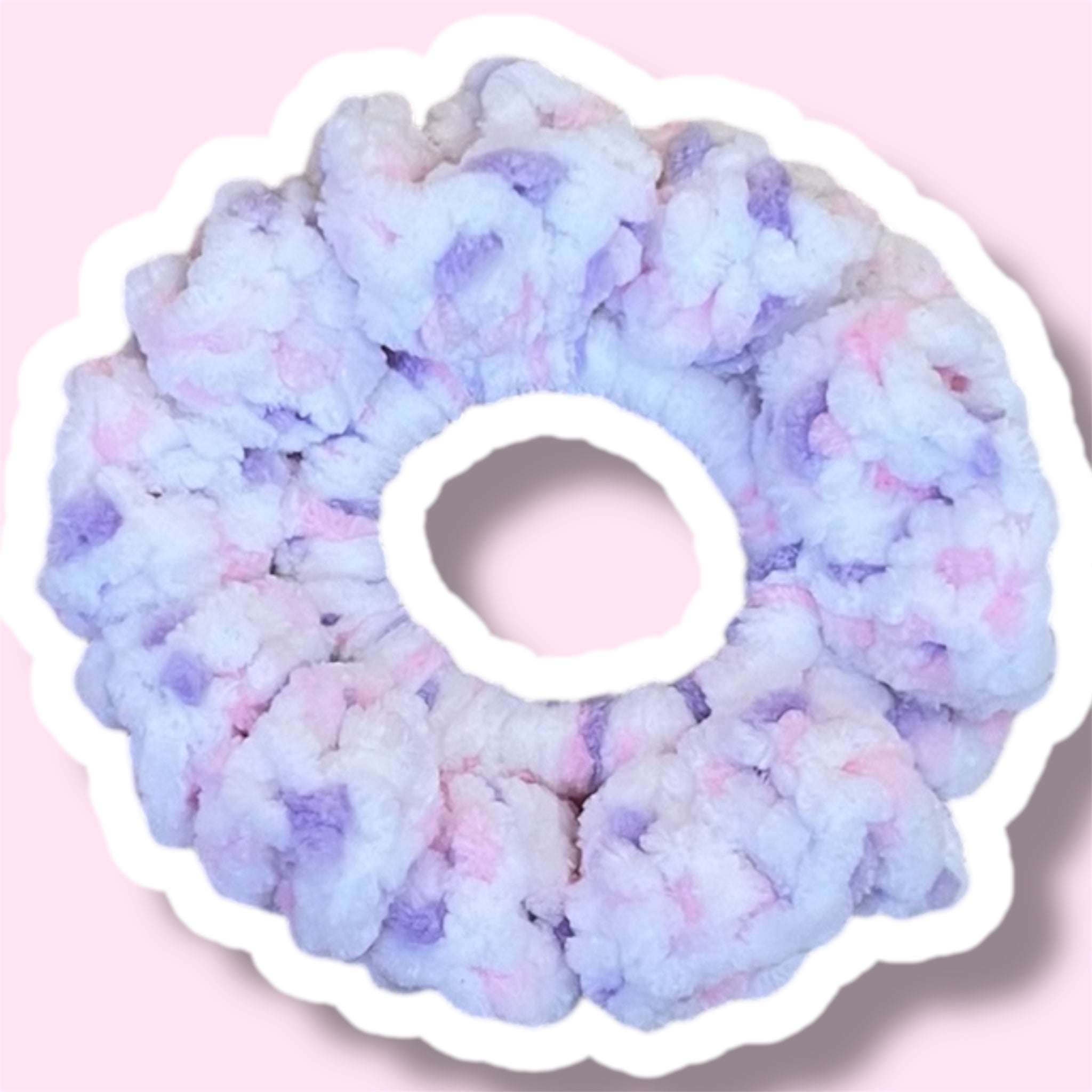 Close up image of a pink and purple handmade crochet scrunchie on a light pink background