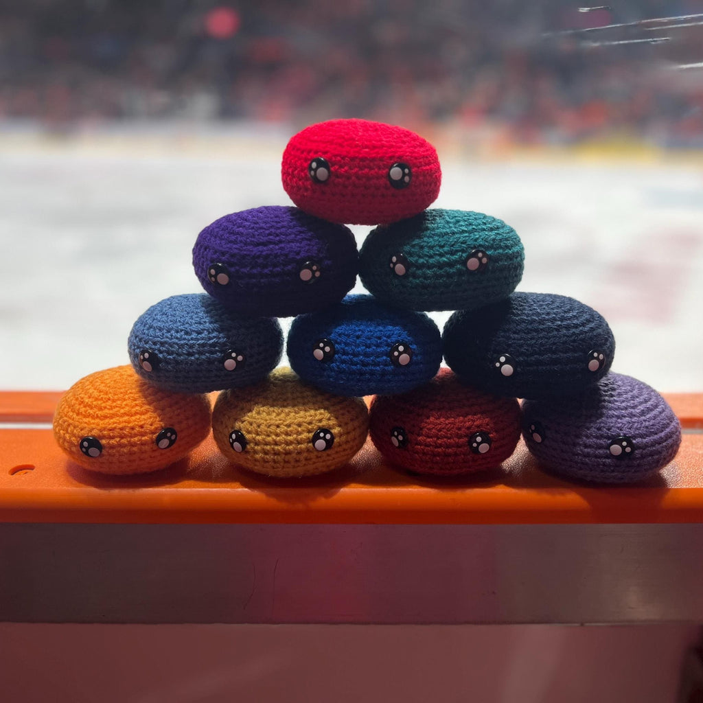 All EIHL team colour crochet ice hockey pucks in a pyramid in front of an ice rink 
