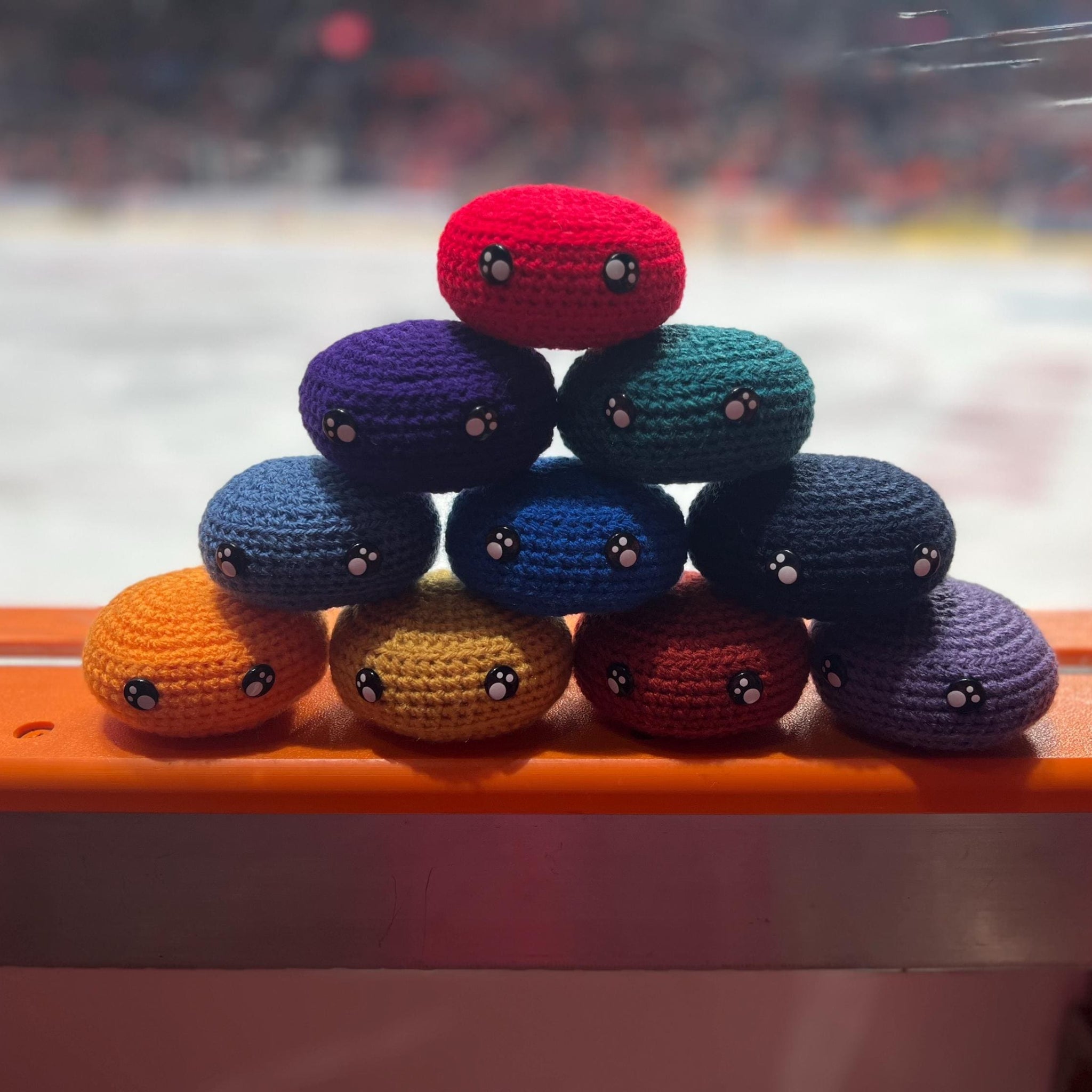 All EIHL team colour crochet ice hockey pucks in a pyramid in front of an ice rink 