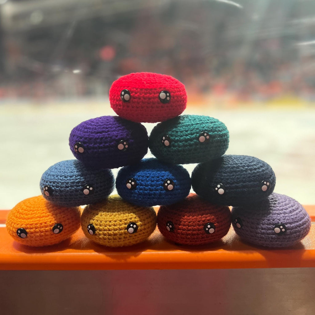 All EIHL team colour crochet ice hockey pucks in a pyramid in front of an ice rink 