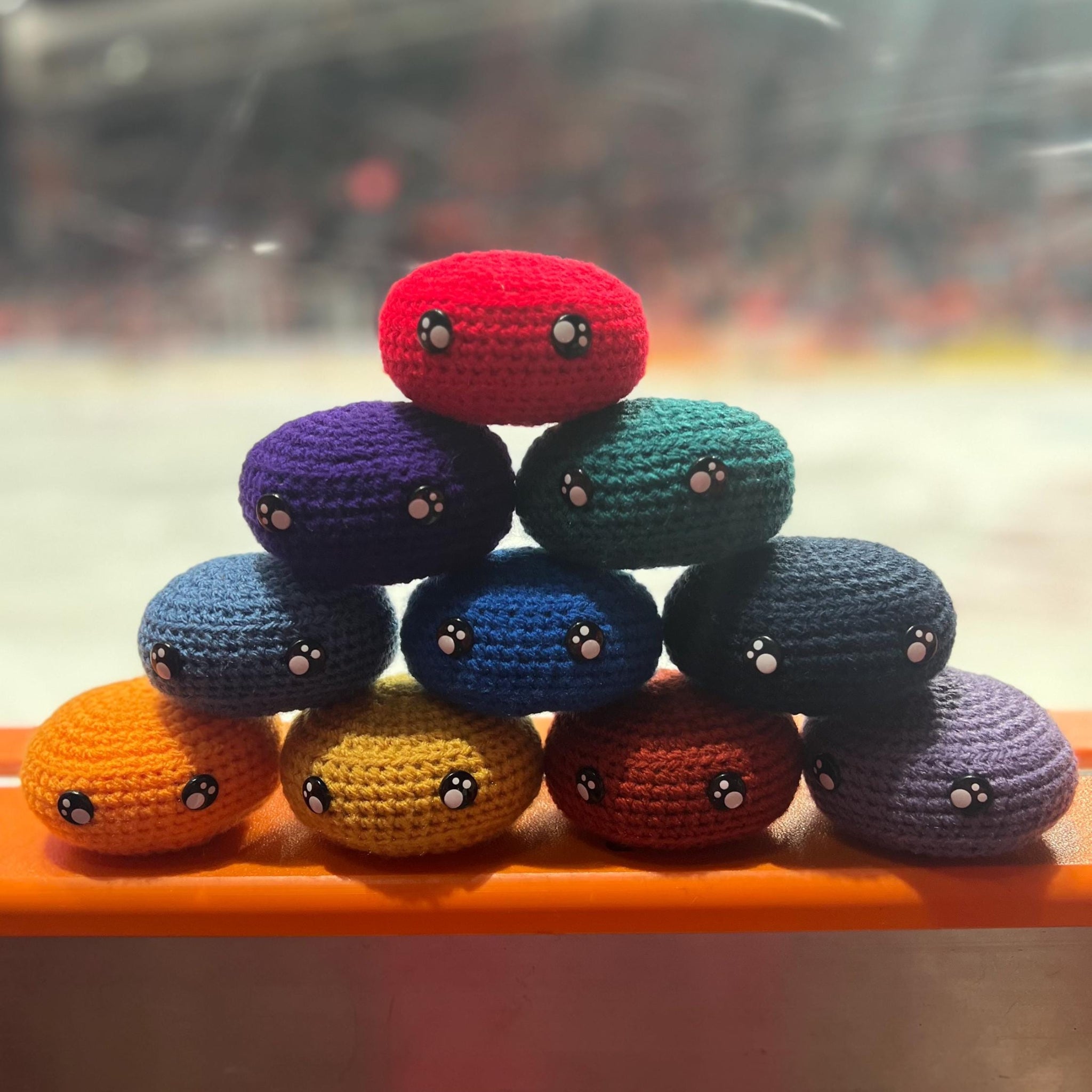 All EIHL team colour crochet ice hockey pucks in a pyramid in front of an ice rink 