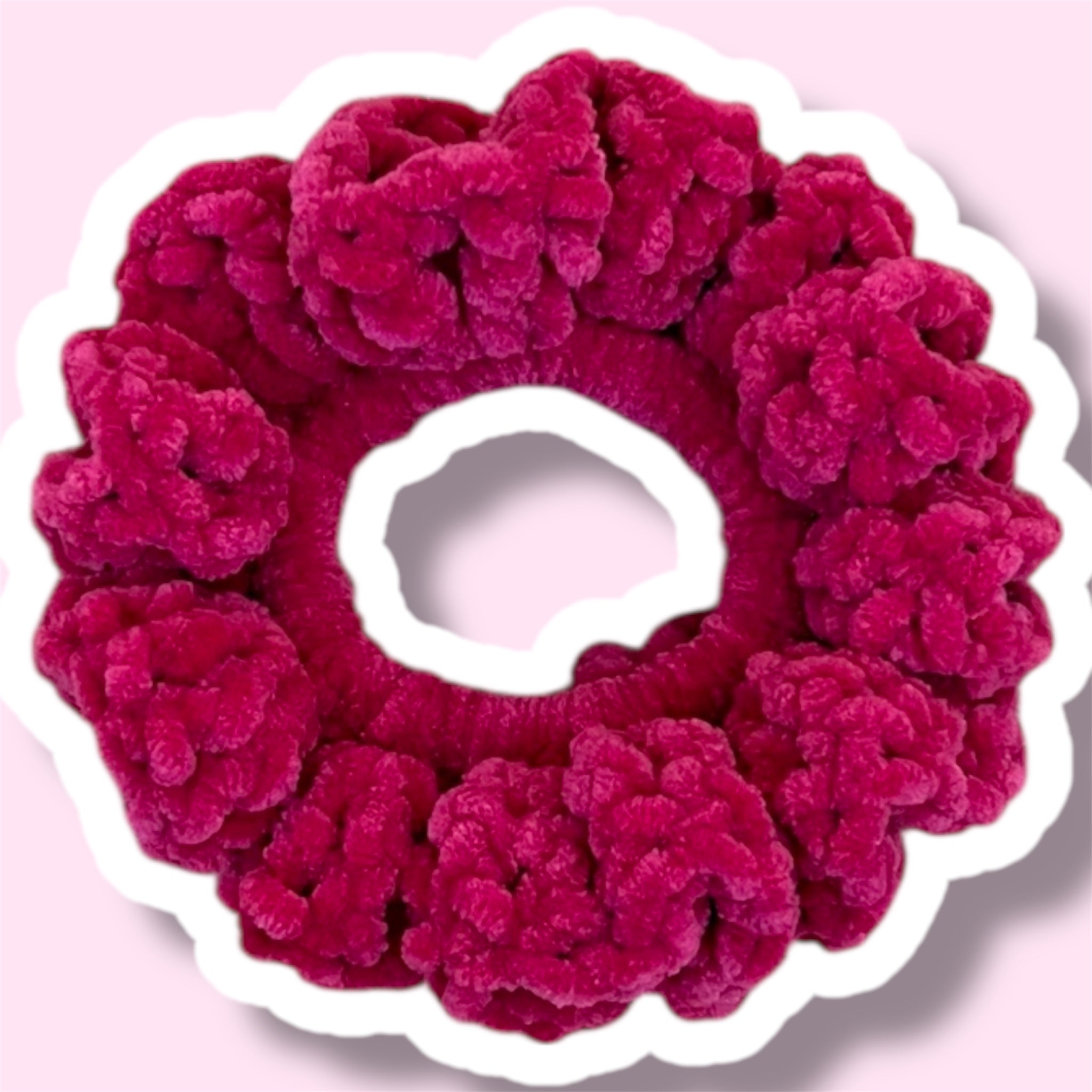 Close up image of a raspberry colour handmade crochet scrunchie on a light pink background
