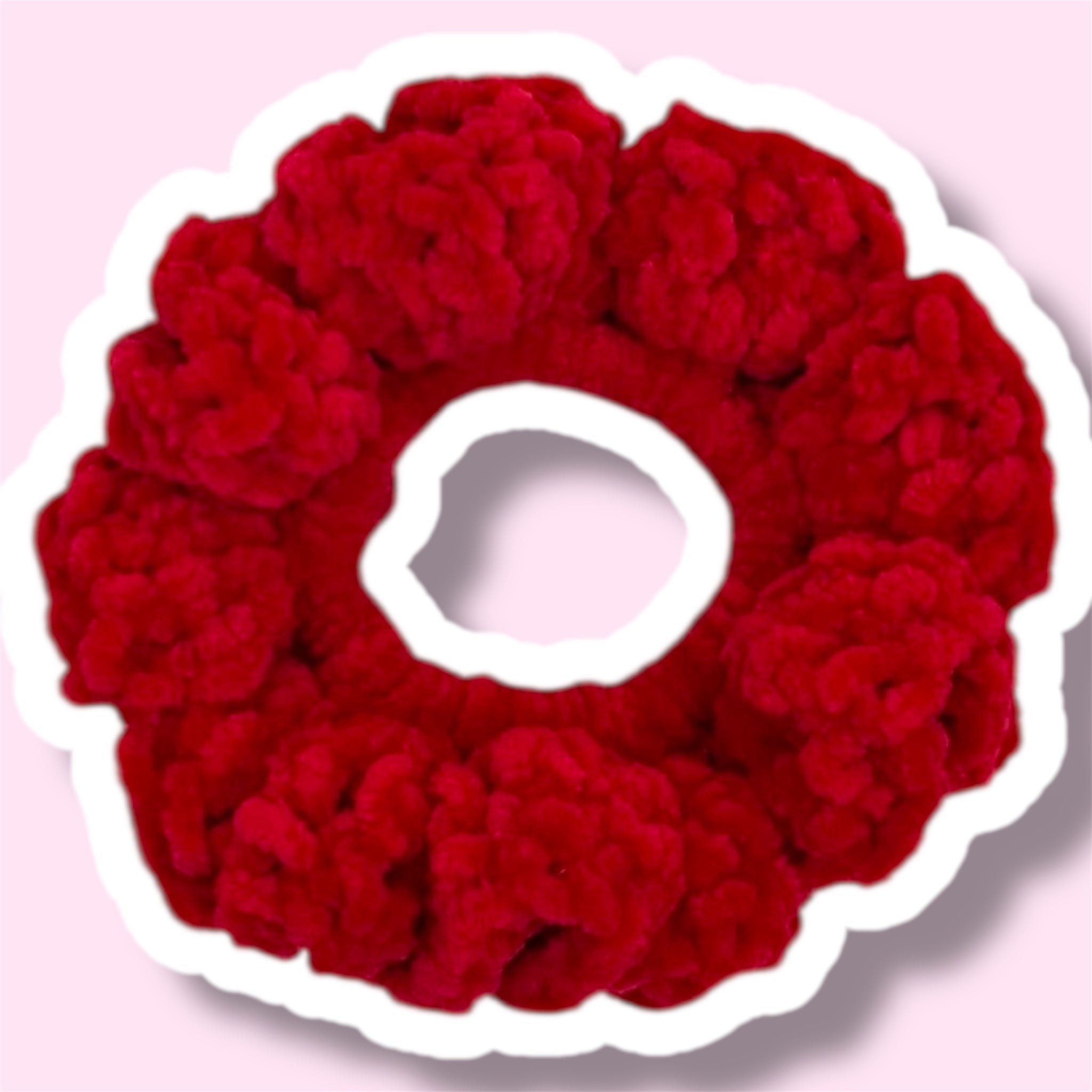 Close up image of a red handmade crochet scrunchie on a light pink background