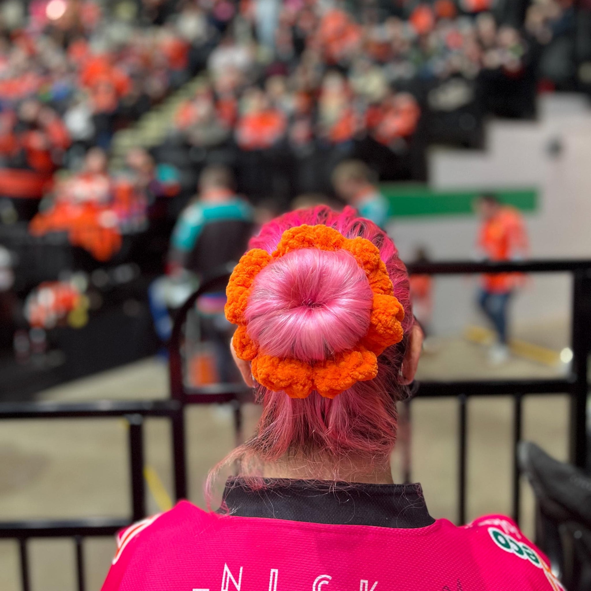 Person wearing an orange sheffield steelers colour themed scrunchie sitting in the stands of an ice hockey game
