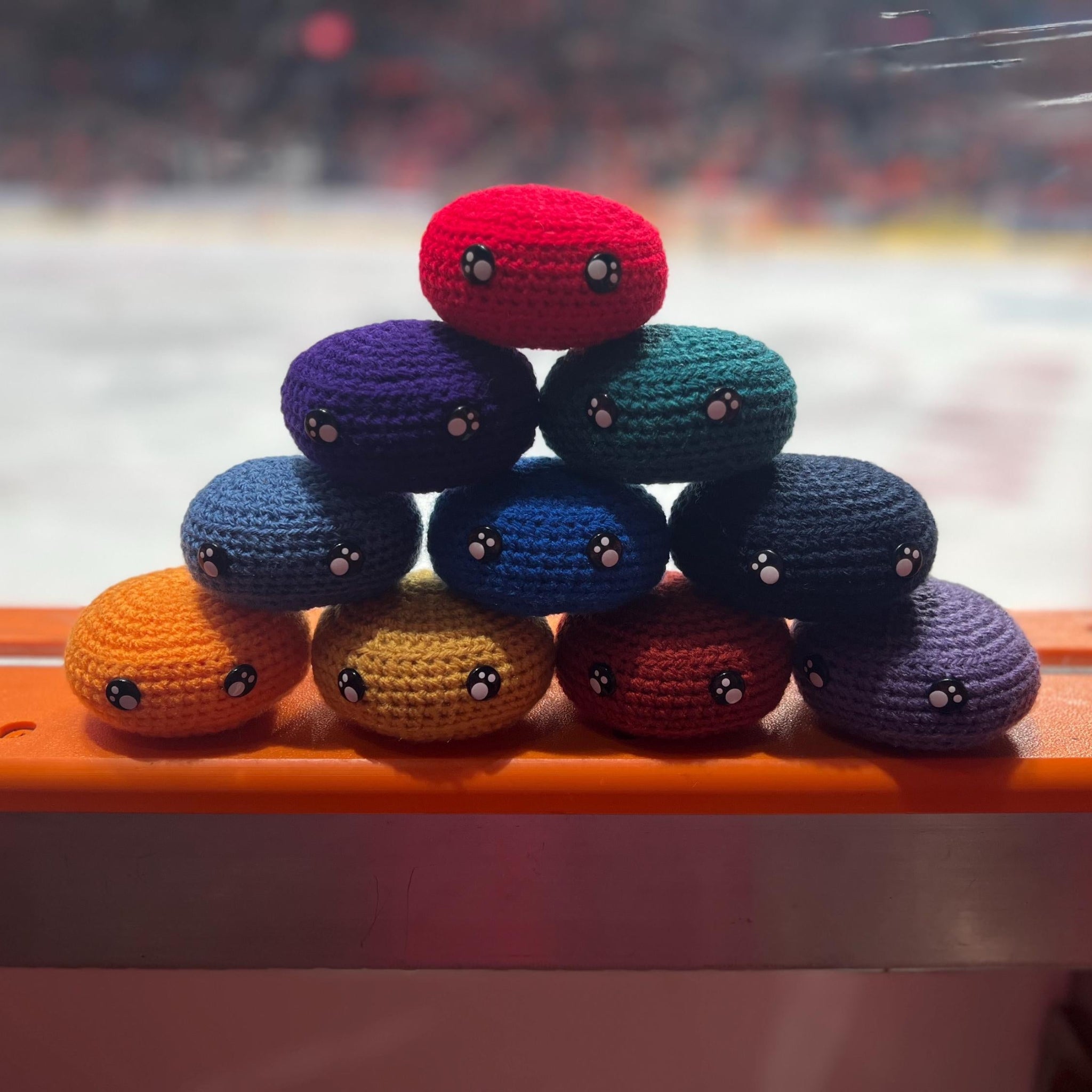 All EIHL team colour crochet ice hockey pucks in a pyramid in front of an ice rink 